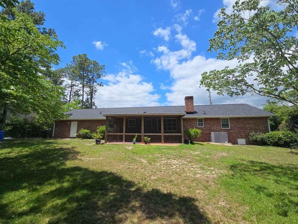 Brick house with a spacious screened porch, surrounded by green lawn and trees under a cloudy sky.