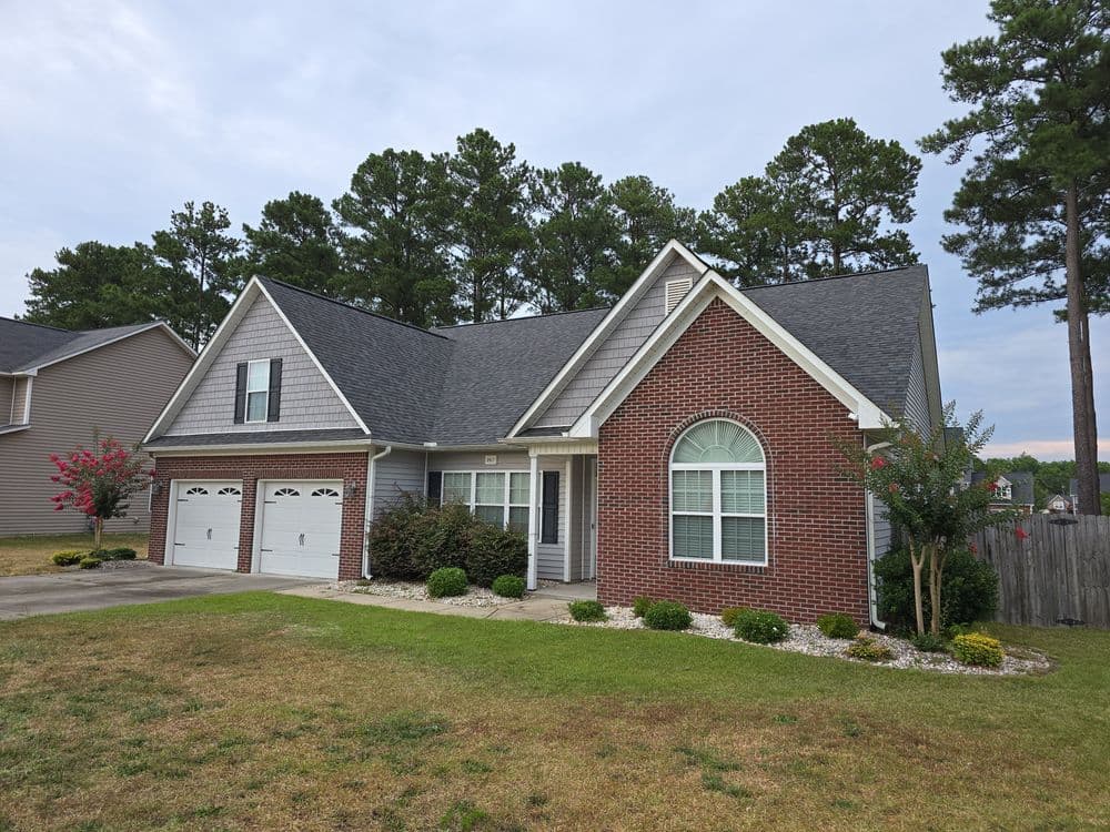 Brick home with a landscaped yard, garage, and trees in the background on a cloudy day.