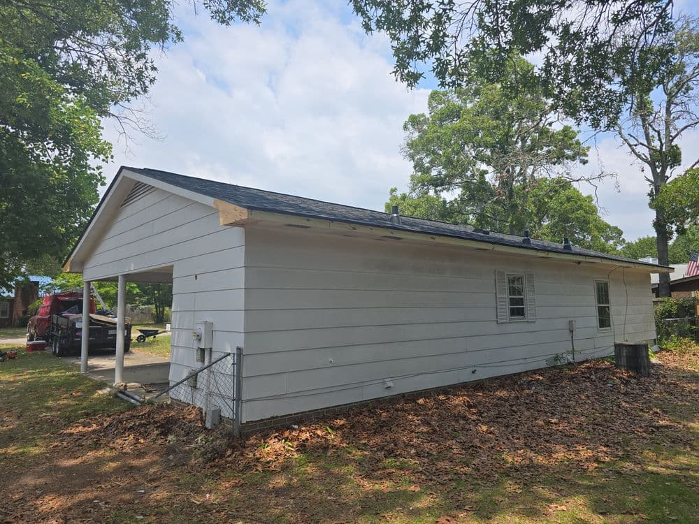 Side view of a single-story house with a carport, surrounded by trees and fallen leaves.