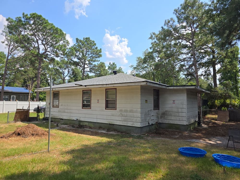 Single-story house with a backyard, surrounded by trees and blue sky. Ideal for renovations or gardening.