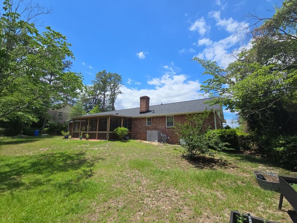 Brick house with porch surrounded by greenery under a partly cloudy sky.