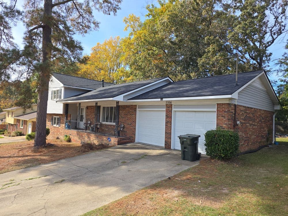 Red brick house with a two-car garage and a driveway, surrounded by autumn trees.